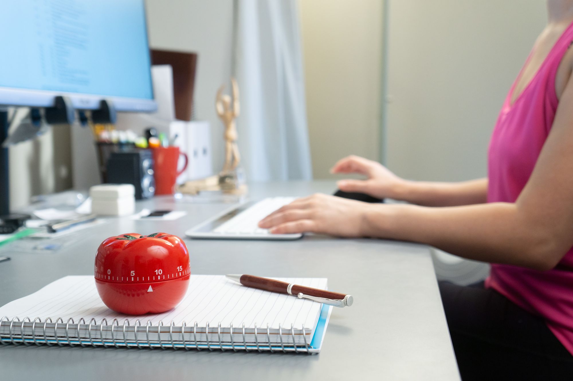 A Pomodoro timer on top of an open notebook, with a person in the background using a computer
