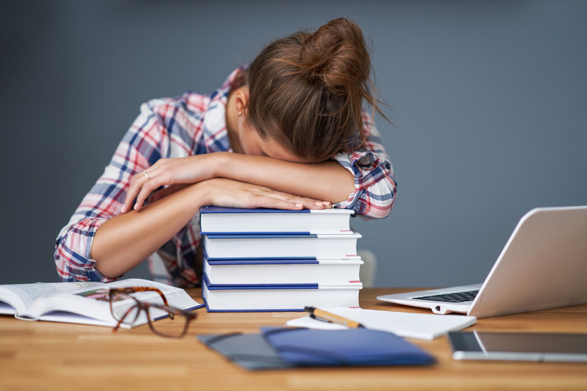 tired female student feeling burn out with head resting on a pile of books