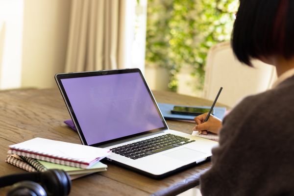 Female student taking notes in a notebook while studying with a laptop at her desk